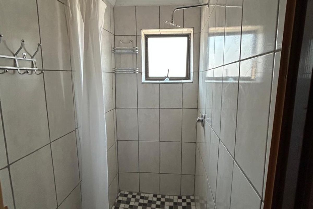 A compact shower cubicle featuring tiled walls, a checkered floor pattern, and a built-in shower head.