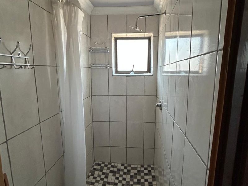 A compact shower cubicle featuring tiled walls, a checkered floor pattern, and a built-in shower head.