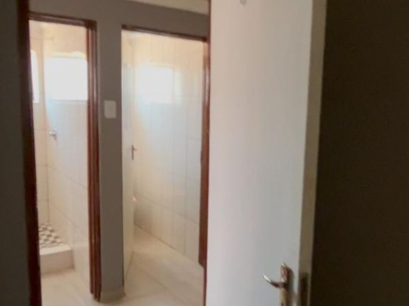 A view of a hallway leading into tiled bathroom or utility spaces, featuring standard internal doors and neutral wall finishes.