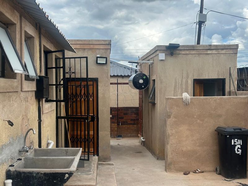 Rear exterior area featuring a concrete laundry sink, security gates, and external geyser unit against a rendered wall finish.
