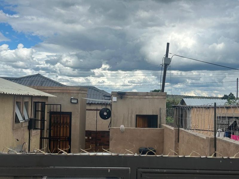 Rear exterior view of the property featuring security fencing, metal roofing, and external wall finishes under a cloudy sky.