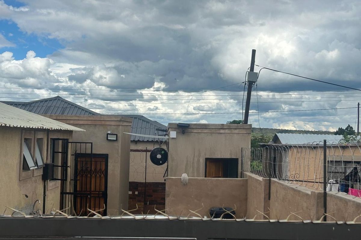Rear exterior view of the property featuring security fencing, metal roofing, and external wall finishes under a cloudy sky.