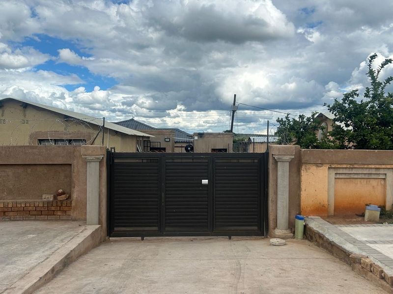 Front view of the property featuring a secure metal driveway gate, perimeter wall with razor wire, and a concrete driveway.