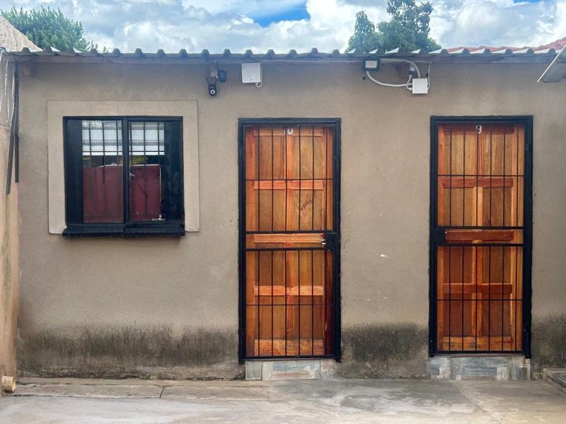 Exterior view of a building facade featuring two timber doors with security gates and a window with security bars, showing signs of rising damp.