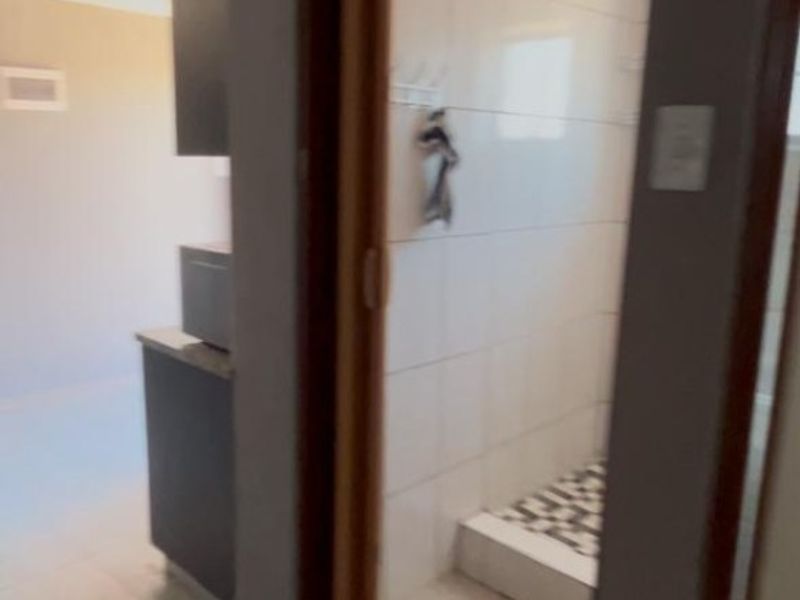 A view of a bathroom featuring tiled walls and flooring, viewed from an adjacent hallway area.