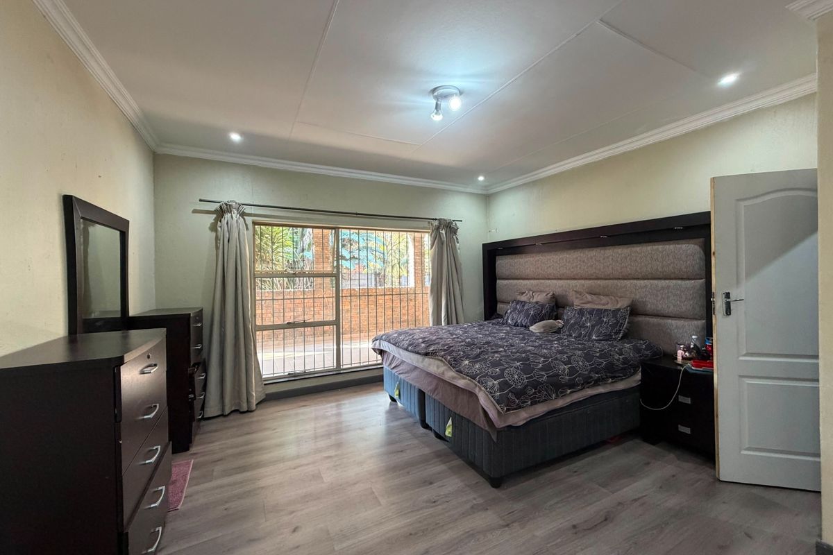 Spacious bedroom featuring modern laminate flooring, recessed ceiling lighting, decorative coving, and a large window fitted with security bars.