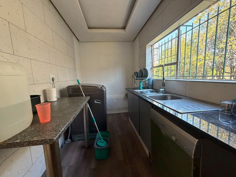 Functional laundry area featuring granite countertops, stainless steel sink, integrated dishwasher, and ample cabinetry with security bars on the window.