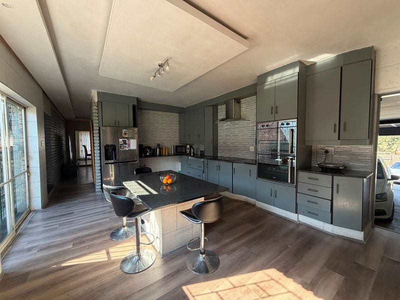 Modern kitchen featuring dark grey cabinetry, granite countertops, a central island, and integrated appliances, with direct access to an outdoor area.