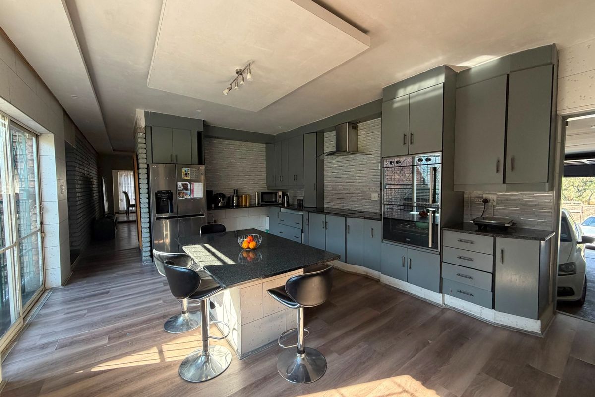 Modern kitchen featuring dark grey cabinetry, granite countertops, a central island, and integrated appliances, with direct access to an outdoor area.