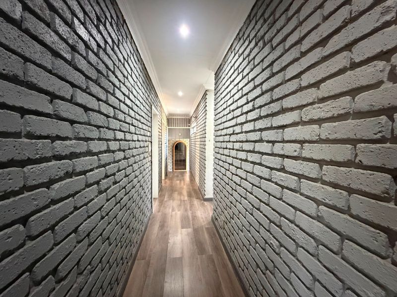 A well-lit hallway featuring distinctive grey exposed brick walls and modern wood-look laminate flooring, creating a clean and contemporary transition space.