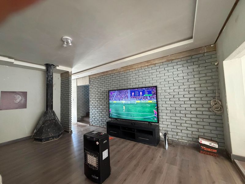 Living room featuring an exposed brick wall, laminate flooring, and a freestanding fireplace, currently requiring some finishing touches to the wall edges and trim.