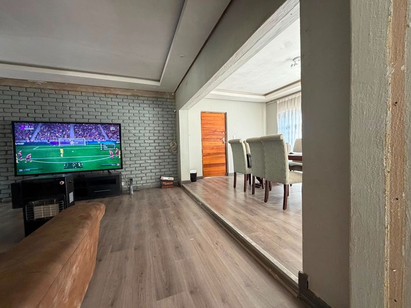 Open plan living and dining area featuring laminate flooring, a painted brick feature wall, and recessed ceiling details with unfinished door trim.