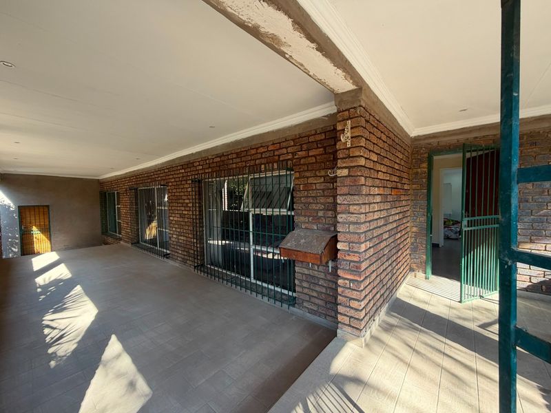 A covered patio area featuring exposed brick walls, tiled flooring, and security bars on windows, providing a functional outdoor space.