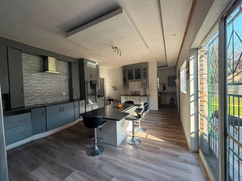 Modern kitchen featuring dark cabinetry, a central island with granite countertops, built-in oven, extractor fan, and laminate flooring with direct access to the patio.
