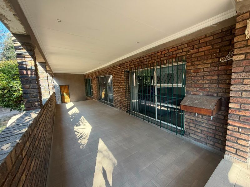 A covered outdoor patio featuring exposed brick walls, tiled flooring, and security bars on the windows, providing a functional and sheltered entrance area.