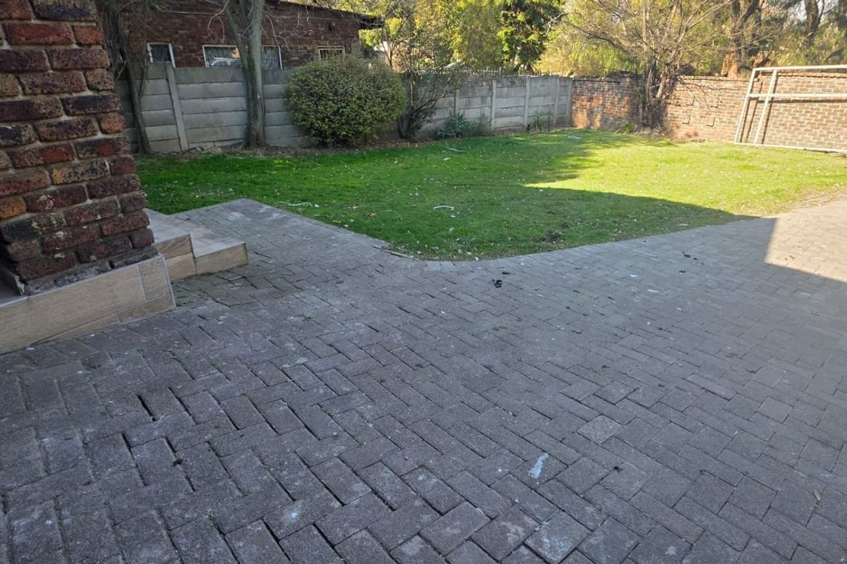 A rear garden area featuring brick paving, a lawn, and perimeter boundary walls.