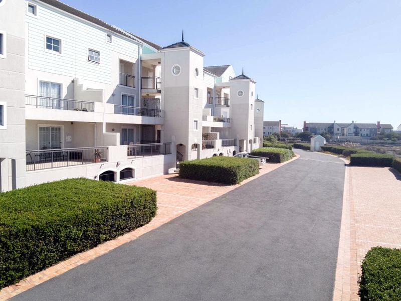 Exterior view of a multi-story apartment complex featuring paved driveways, manicured hedges, and private balconies with metal railings.