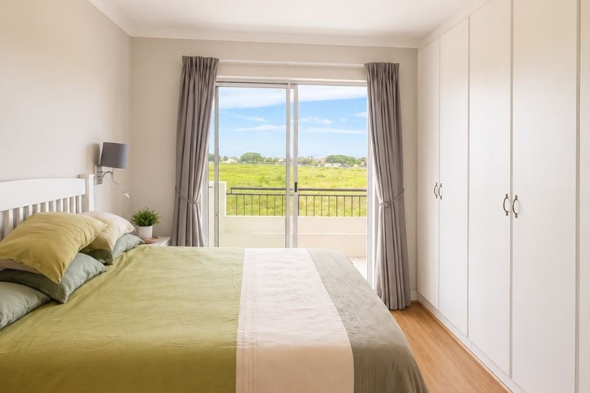 A well-maintained bedroom featuring light laminate flooring, extensive built-in wardrobes, and a sliding glass door providing access to a balcony with scenic views.