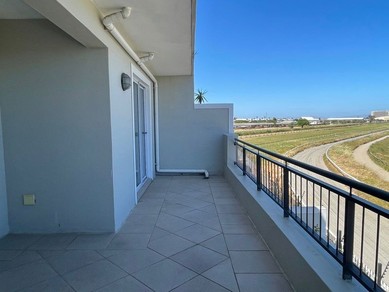 A spacious, clean balcony featuring tiled flooring, a metal balustrade, and an open view of the surrounding landscape.