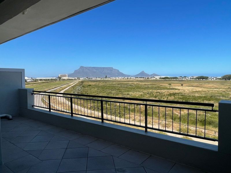 A spacious, clean balcony featuring tiled flooring and a metal balustrade, offering expansive, unobstructed views of the landscape and Table Mountain.