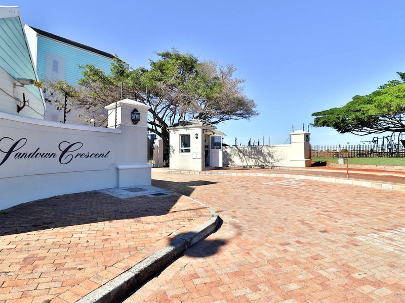 The entrance to Sandown Crescent featuring a paved driveway, secure perimeter walling with electric fencing, and a dedicated security guard house.