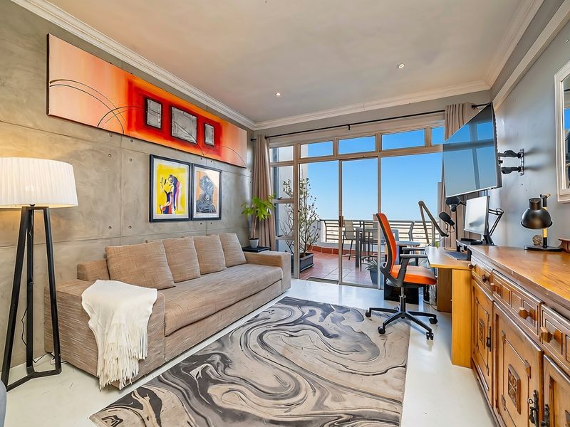 A modern living room featuring a concrete accent wall, crown molding, and large sliding glass doors providing direct access to an outdoor balcony.
