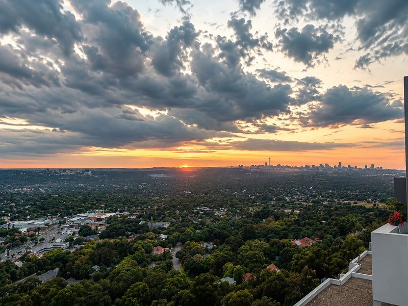 Elevated panoramic sunset view overlooking a lush suburban landscape and distant city skyline from a high-rise apartment balcony.