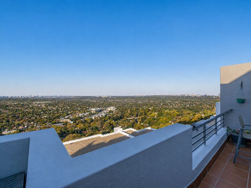 A spacious balcony featuring tiled flooring and a metal railing, offering expansive panoramic views of the surrounding landscape and city skyline.