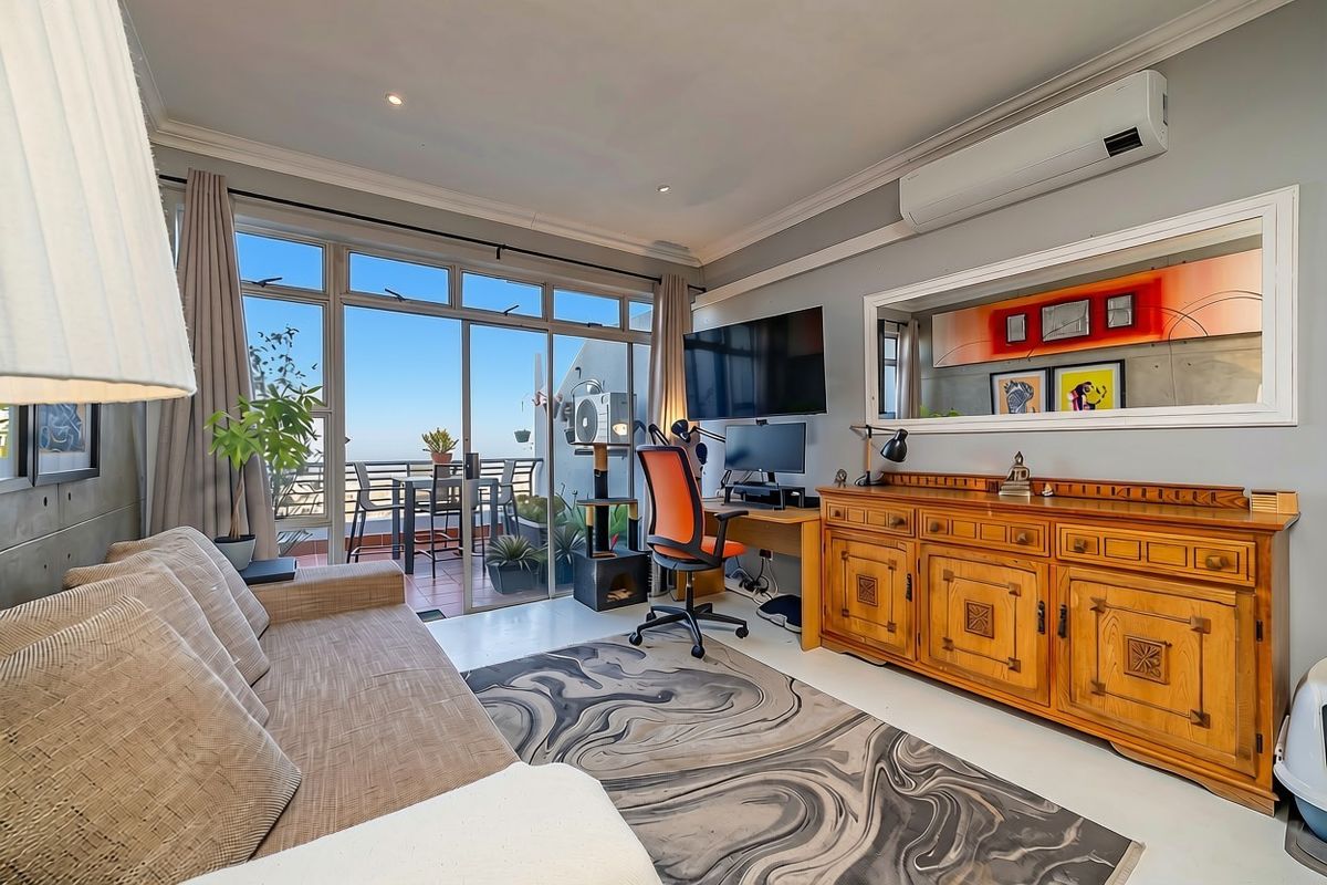 A well-maintained living room featuring a concrete accent wall, split-system air conditioning, and large sliding glass doors providing access to an outdoor balcony.
