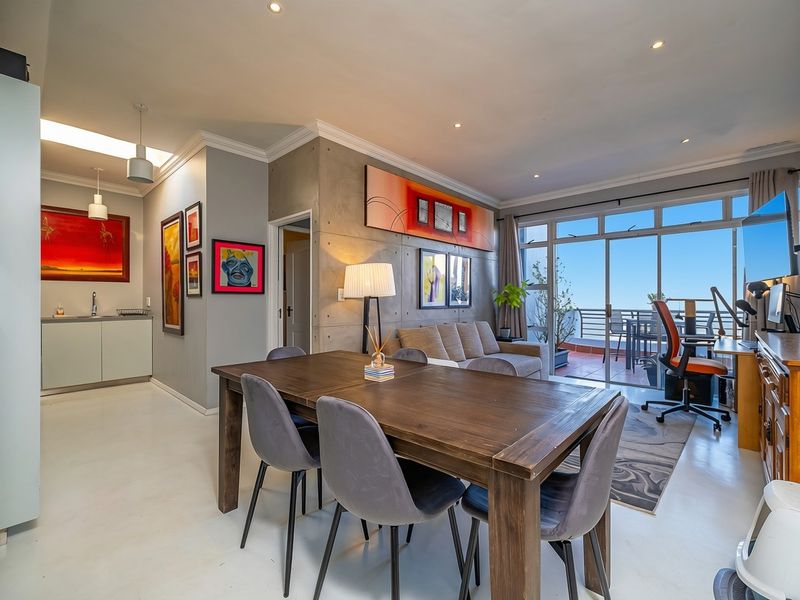 Spacious open-plan living and dining area featuring a concrete feature wall, recessed lighting, and seamless access to a private balcony with scenic views.