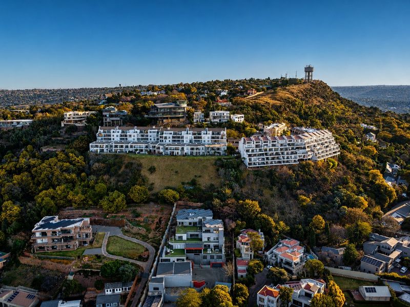 An aerial view of a residential hillside neighborhood featuring multi-story apartment complexes nestled within a landscaped, elevated terrain.