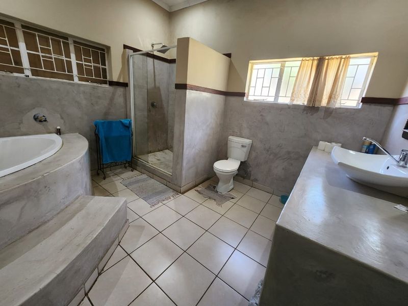 Spacious bathroom featuring a built-in concrete bathtub, walk-in shower, toilet, and a vessel sink set on a concrete vanity with tiled flooring.