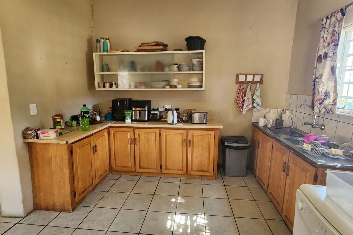 A functional kitchen featuring wooden cabinetry, laminate countertops, a stainless steel double sink, and tiled flooring, offering a practical layout for daily use.