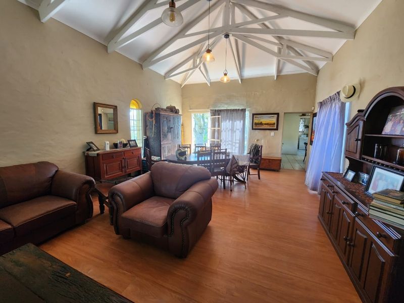 Spacious open-plan living and dining area featuring high vaulted ceilings with exposed timber trusses and warm laminate flooring.