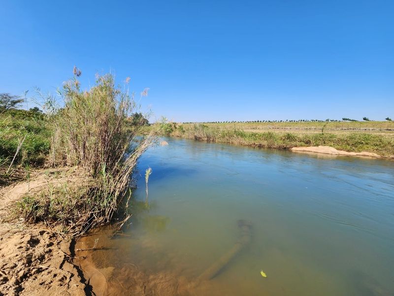 A scenic view of a natural river flowing through the farm landscape with surrounding vegetation.