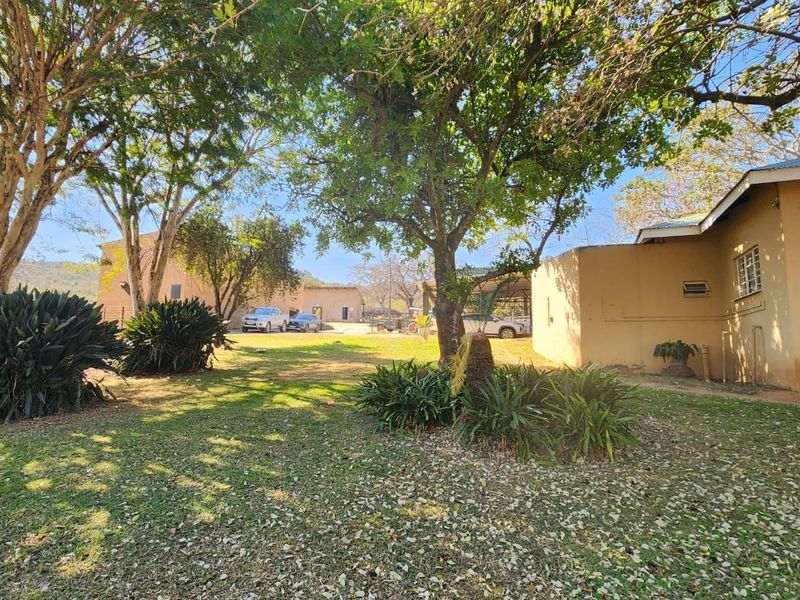 A spacious farm garden area featuring mature trees, established landscaping, and views of the surrounding farm buildings and outbuildings.