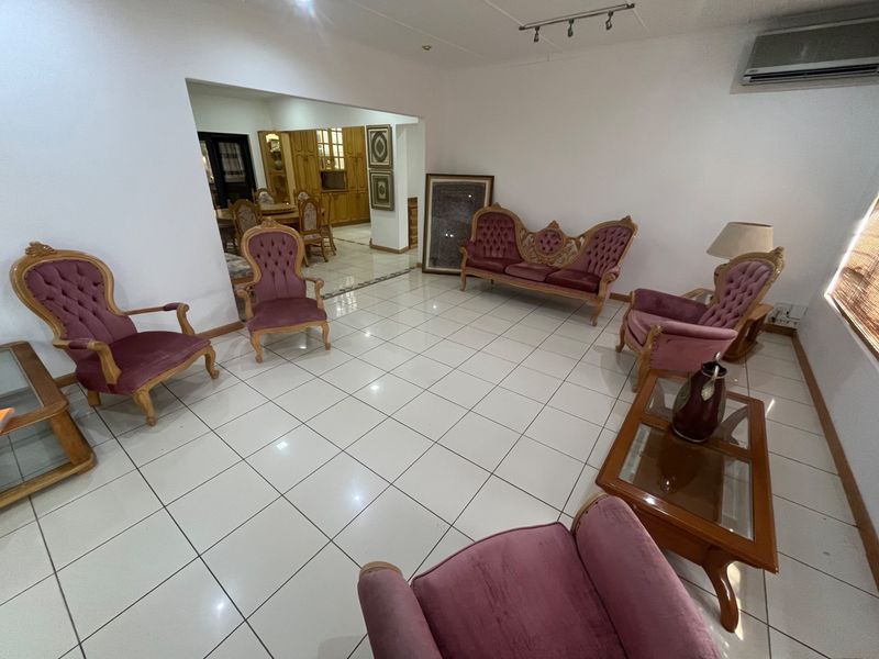 Spacious living area featuring neutral ceramic floor tiles, track lighting, and a wall-mounted split-system air conditioner, with an open-plan flow to the dining area.
