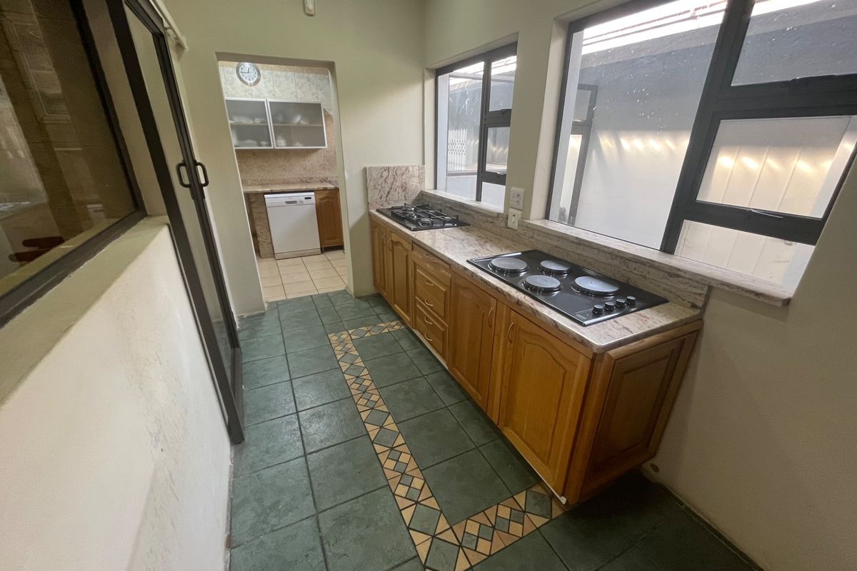 A functional kitchen featuring dual hobs, granite countertops, and wooden cabinetry, with a separate scullery area visible in the background.