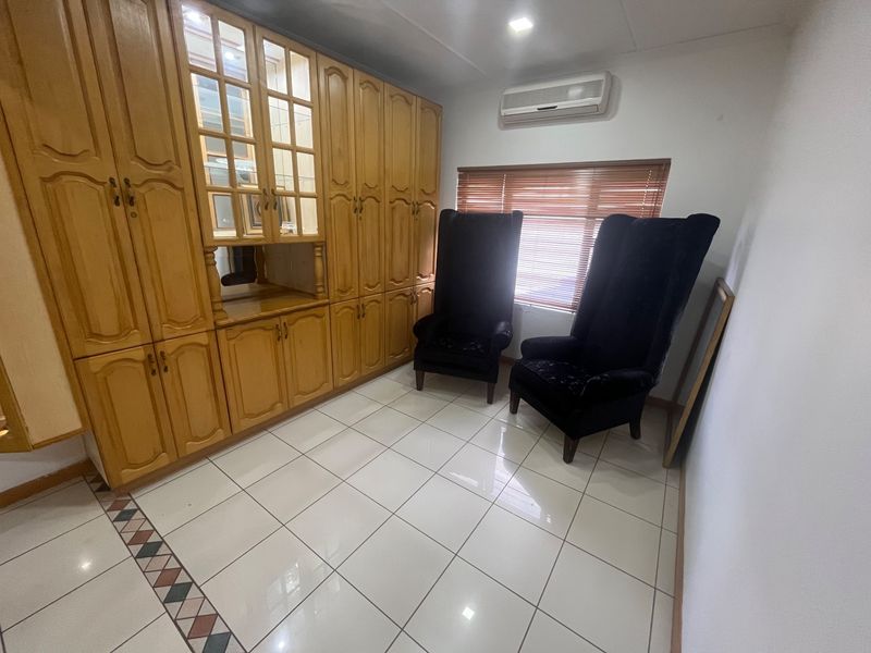 A living area featuring extensive built-in wooden cabinetry, tiled flooring, and a wall-mounted split-system air conditioner.