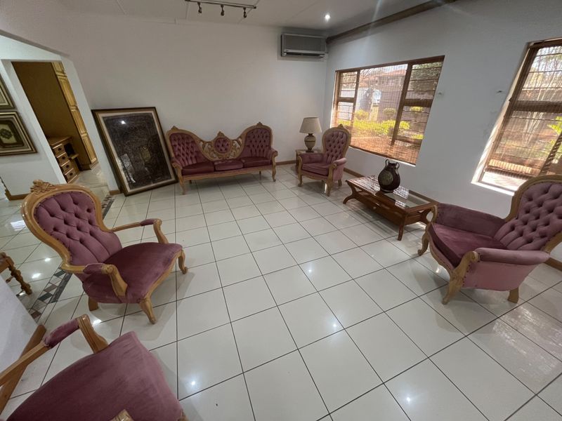 Spacious living room featuring white tiled flooring, large windows providing natural light, and a wall-mounted air conditioning unit.