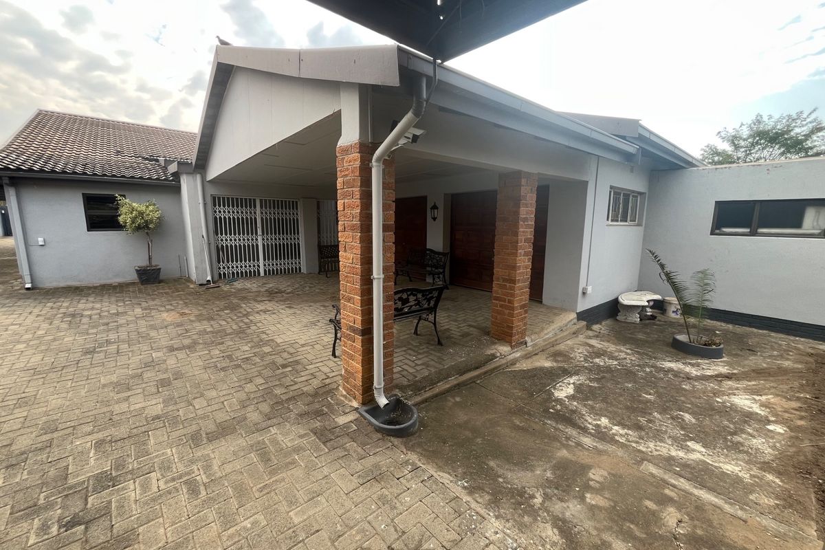 Rear exterior view featuring a covered patio area with brick pillars, paved courtyard, and secure gated access to the main dwelling.