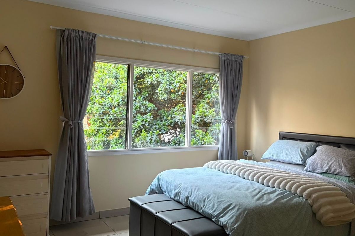 A well-lit bedroom featuring tiled flooring and a large window with garden views, providing a comfortable and functional living space.