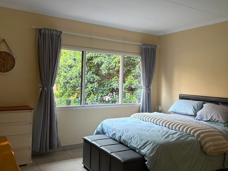 A well-lit bedroom featuring tiled flooring and a large window with garden views, providing a comfortable and functional living space.