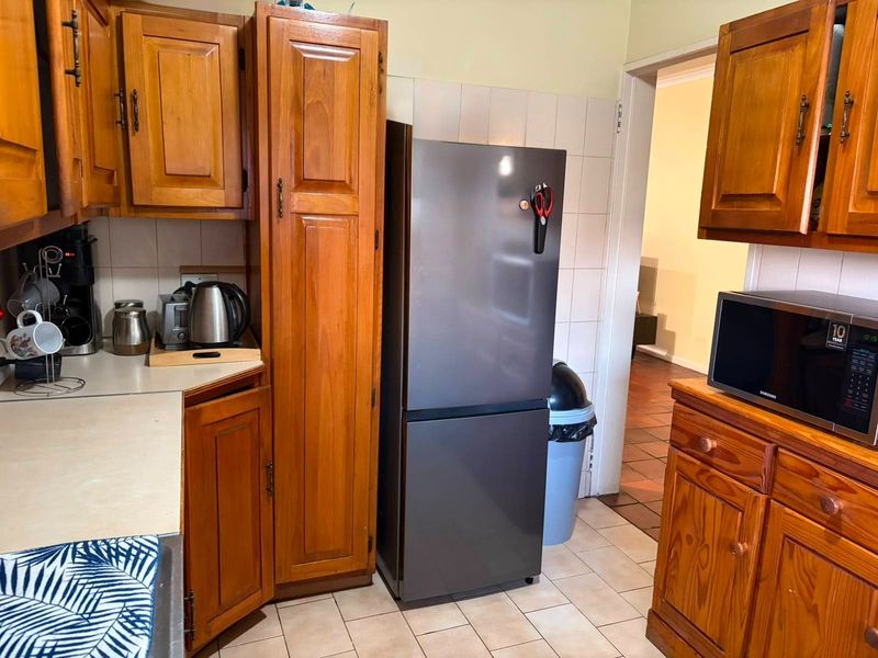 A functional kitchen featuring traditional wooden cabinetry, tiled backsplash, and tiled flooring, offering a classic aesthetic with ample storage space.