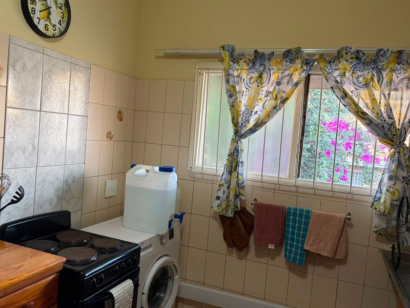 A functional kitchen area featuring a tiled splashback, electric stove, and integrated laundry plumbing, with security bars installed on the window.