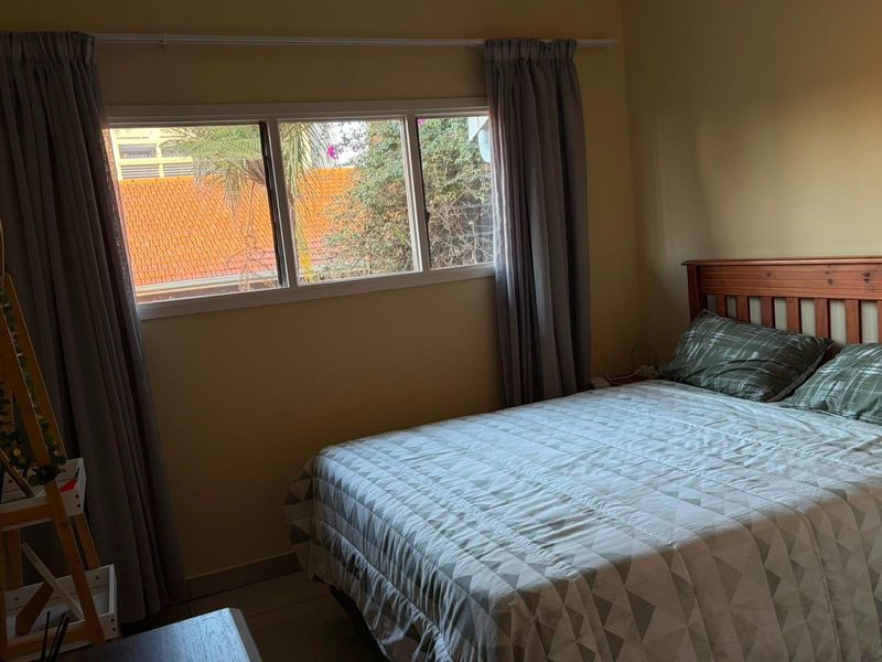 A functional bedroom featuring tiled flooring and a window with curtain tracks, offering a neutral space ready for personalization.
