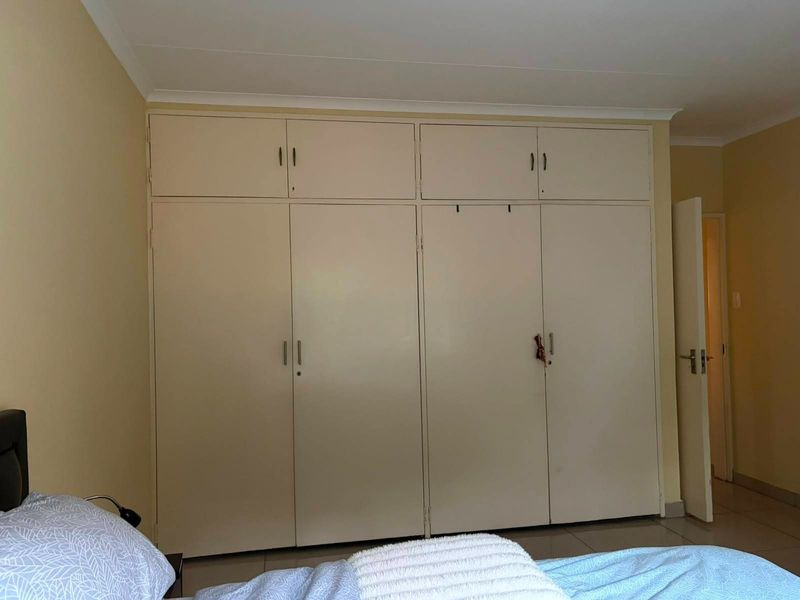 A bedroom featuring extensive floor-to-ceiling built-in cupboards providing ample storage space, complemented by neutral wall finishes and tiled flooring.