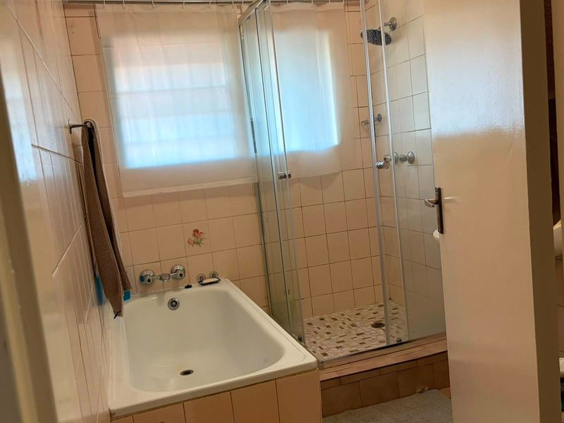 A functional bathroom featuring a built-in bathtub and a separate glass-enclosed shower with tiled finishes throughout.