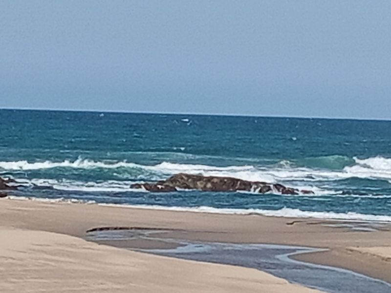 A scenic view of the ocean, sandy beach, and rocky shoreline, highlighting the natural coastal landscape of the property.