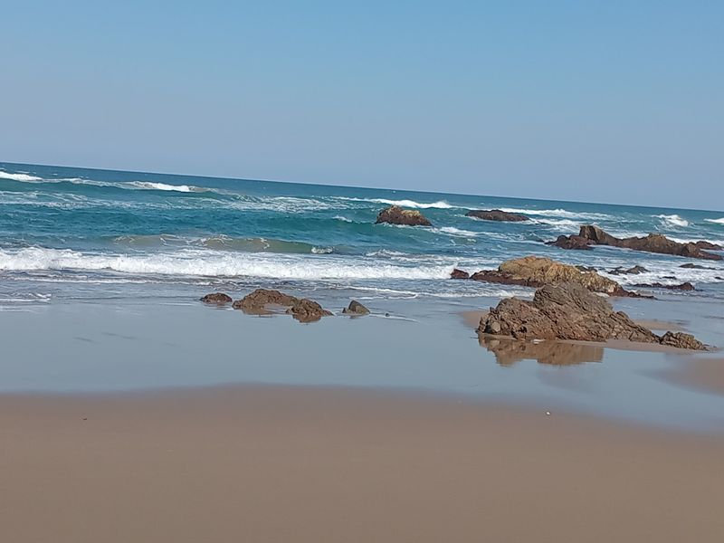 A scenic view of the ocean coastline featuring sandy shores and rocky outcrops.